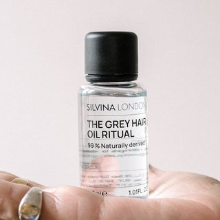 Hand holding a small bottle labeled 'The Grey Hair Cultivator' against a plain background