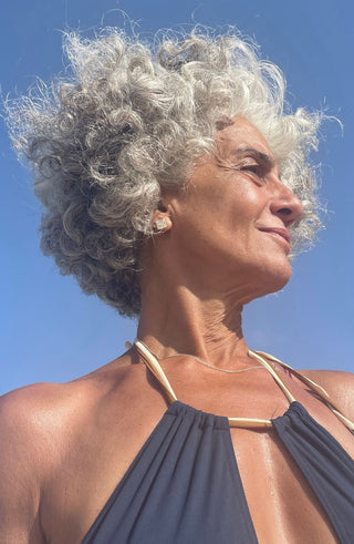 Woman with grey hair wearing a blue swimsuit against a clear blue sky