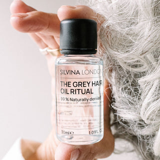 Silvina London grey hair oil ritual bottle held by a hand with gray hair.