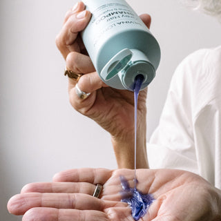 Person pouring blue shampoo from a Silvina LONDON bottle into their palm against a neutral background